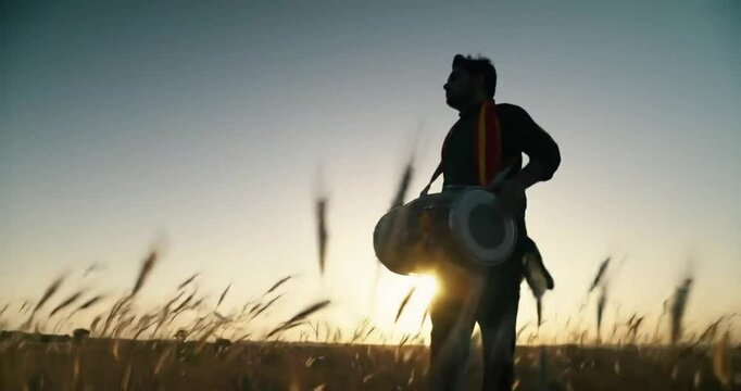 Silhouette of a musician holding a traditional dhol drum in a golden wheat field at sunset, embodying cultural heritage.