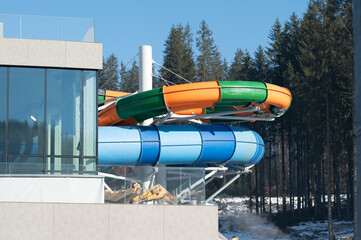 Colorful water slides twist and turn beside a modern building in a winter landscape with...