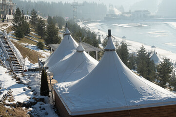 Winter wonderland retreat with snowy tents beside tranquil lake nestled in mountains at dawn...