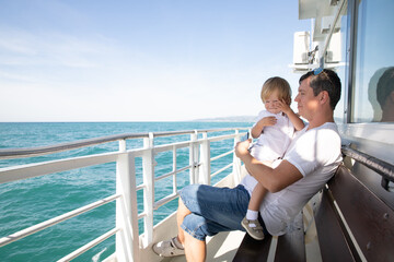 A man and a boy on a white boat in the sea are sitting by the side, father and son are enjoying a sea trip