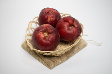 Three red Jamaican guavas in a wicker basket are placed on burlap, against a white background.