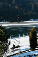Winter adventure unfolds as a thrill-seeker ziplines across a serene frozen lake beneath towering...