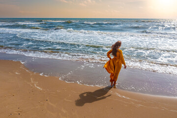 Seascape on a sunny day. Woman on the beach. Young woman in a yellow fluttering dress stands on the...