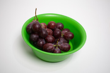 A bunch of fresh red grapes in a bright green bowl on a white background.