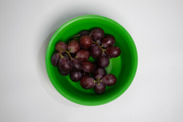 Juicy purple grapes arranged in a vibrant green plastic bowl.