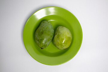 Two fresh green mangoes on a matching green plate, placed on a clean white surface.