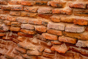 A close-up of a beat-up red brick wall with rough, uneven bricks in shades of red, orange, and brown, showing off years of wear and tear.