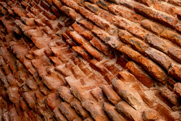 A close-up of a beat-up red brick wall with rough, uneven bricks in shades of red, orange, and...