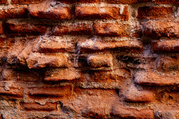 A close-up of a beat-up red brick wall with rough, uneven bricks in shades of red, orange, and...