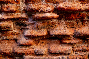 A close-up of a beat-up red brick wall with rough, uneven bricks in shades of red, orange, and...