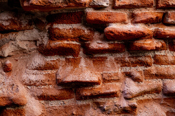 A close-up of a beat-up red brick wall with rough, uneven bricks in shades of red, orange, and...
