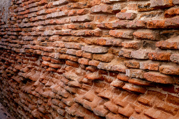 A close-up of a beat-up red brick wall with rough, uneven bricks in shades of red, orange, and...