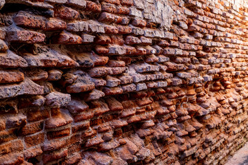 A close-up of a beat-up red brick wall with rough, uneven bricks in shades of red, orange, and...