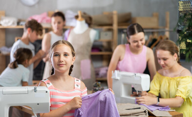 Engaged tween girl enjoying relaxed sewing workshop for children led by professional seamstress,...