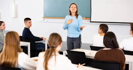 Positive adult female teacher leading a lecture in the classroom