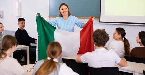 High school teacher tells students about Italy and holds a Italy flag in her hands.