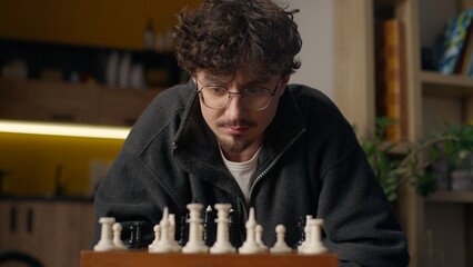 Focused Hispanic guy player playing chess mind game at home hipster look chessboard thinking...