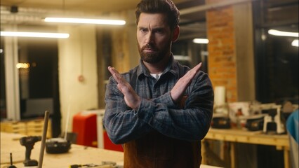 Serious Caucasian wood master man show prohibition gesture in workshop craftsman forbid builder joiner rejection guy demonstrating cross with hands male repairman ban no symbol artist decline refusing