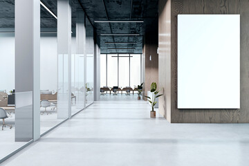 Modern office hallway with vertical blank canvas display on wood wall and open workspace with glass...