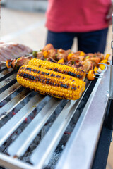 Grilled corn on the cob with barbecue ribs and chicken skewers grilling in background