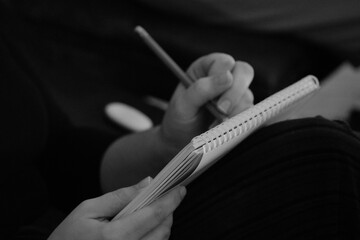 Art student holds spiral-bound notebook and pencil sketching. Drawing picture emphasizes texture of...