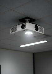 White projector mounted to the ceiling of an office space. Suspended projector in a modern, neutral office environment.