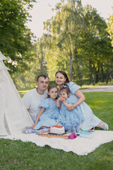 A happy family on a picnic. The family has two daughters. The family is dressed in blue clothes,...