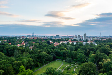 Aerial panorama of lush green park and distant cityscape under cloudy sunset sky