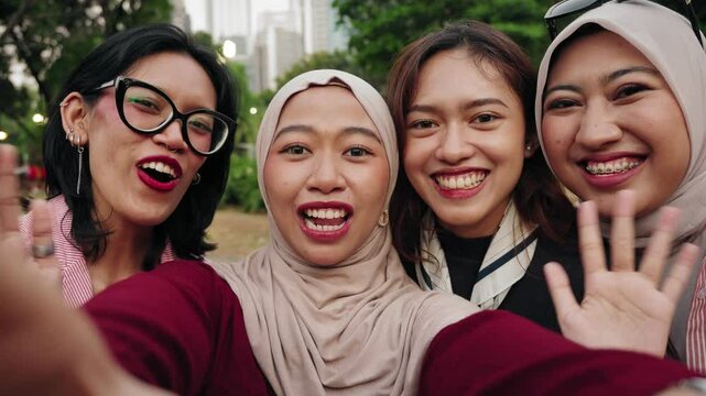 Three asian Indonesian women friends are taking selfie picture in a park using mobile phone