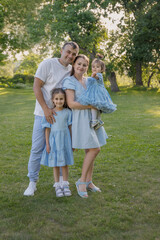 Fototapeta premium A happy family in nature. The family has two daughters. The family is dressed in blue clothes, and everyone is looking at the camera. 