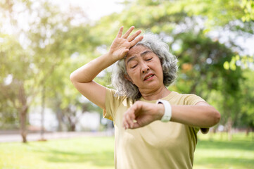 Old woman looking at the wristwatch while wiping her sweat after finish exercise in time at the park