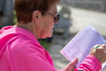 senior woman doing crossword puzzles relaxing sitting on the street