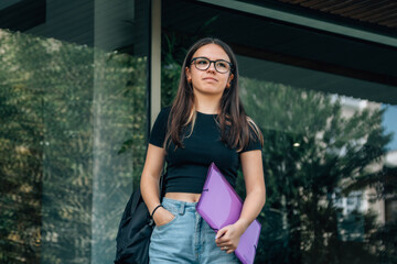 teenage girl student in front of school with folder and backpack