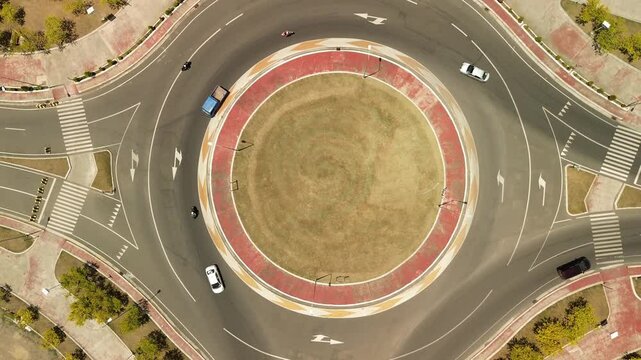Drone climbs straight up over a perfectly circular seaside roundabout in Davao City, capturing orderly vehicle flow, red-rimmed asphalt and crisp midday light.