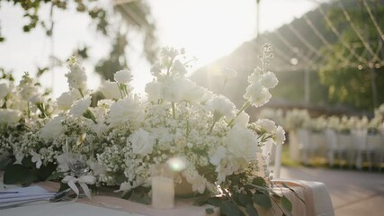 Elegant white floral arrangement on a wedding table in natural sunlight. Ideal for wedding, romance, event planning, floral decor, and luxury celebration themes.