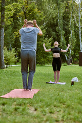 Young caucasian male and female performing qigong in lush park. Sunlit, serene ambiance adds calm....