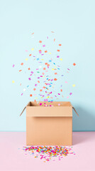 Colorful Confetti Falling into an Open Cardboard Box Against a Soft Pink Background