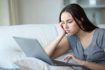 Bored woman checking bad content on laptop at home