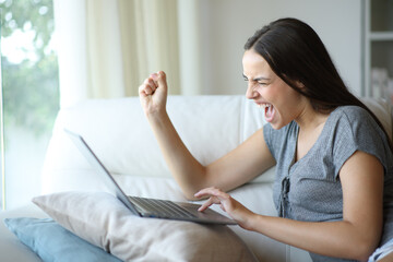 Excited woman celebrating good news is checking laptop