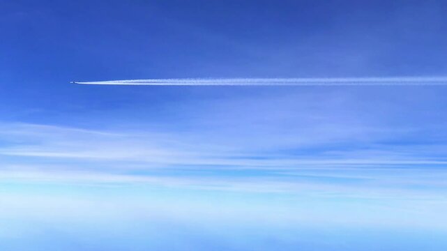 Aerial view of a clear blue sky with soft clouds and a jet contrail creating a striking visual contrast, evoking a sense of freedom and tranquility in the atmosphere 