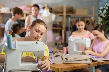 Teenage girl works on sewing machine while teacher and students learn how to cut fabric
