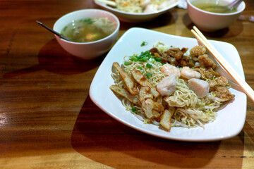 Dried noodles with various toppings including fish cakes, shrimp, and crispy pork, served with a side of clear soup.