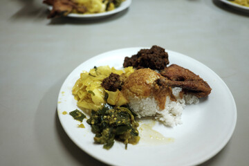 A delicious Nasi Padang plate featuring rice with gulai sauce, gulai cabbage, fried chicken drumstick, flavorful beef rendang, and spicy green chili sambal.
