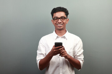 Happy young teenager of Indian origin holding a mobile phone in hand