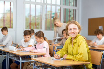 Fototapeta premium Portrait of smiling positive schoolgirl posing in classroom during lesson in secondary school