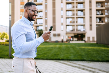 Businessman checking messages on his smartphone while walking in an urban setting with modern...