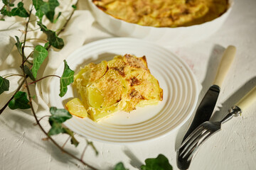 Delicious graten made with layers of sliced potatoes and cheese in a white rustic kitchen setting
