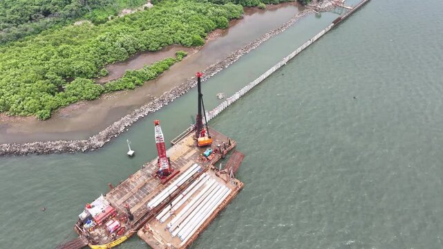 aerial view of the process of installing a giant sea wall by a large drilling machine on the north coast of Java Island