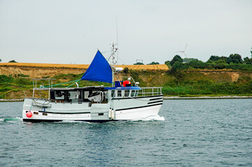 A fishing boat with a blue sail glides through serene waters, surrounded by lush green hills during...