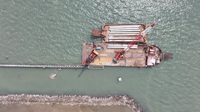 aerial view of the process of installing a giant sea wall by a large drilling machine on the north coast of Java Island